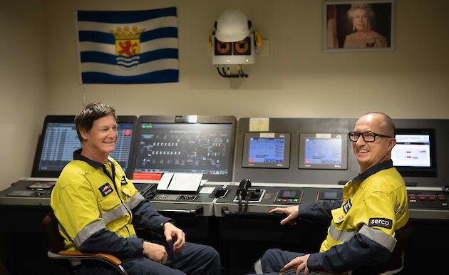 Two men sit at the controls in the engine room