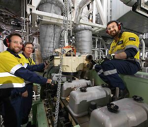 Three men working on a large ship's engine