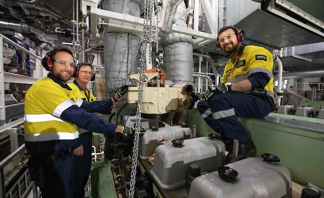 Three men working on a large ship's engine