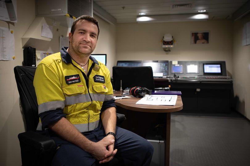 A man in hi vis sits at a desk in a control room and smiles to camera