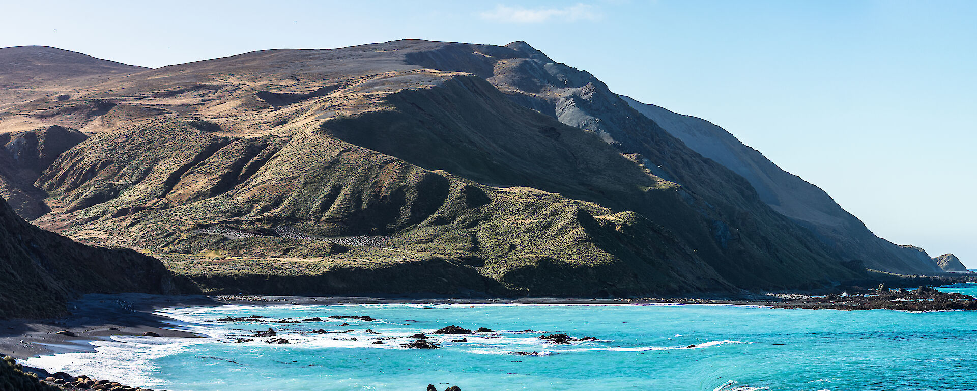 Blue water in the bay below a large grassy hill