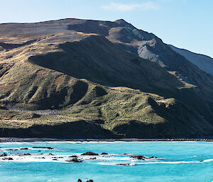 Blue water in the bay below a large grassy hill