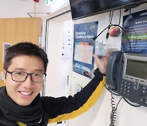 A man in glasses stands next to a wall telephone