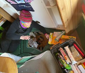 An expeditioner laying on the floor next to the underfloor opening from where they are pulling out packets of food.