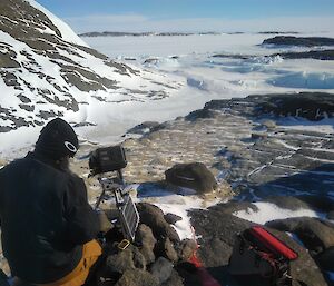 A man working on the fixed bird camera on a rocky outcrop above the sea ice
