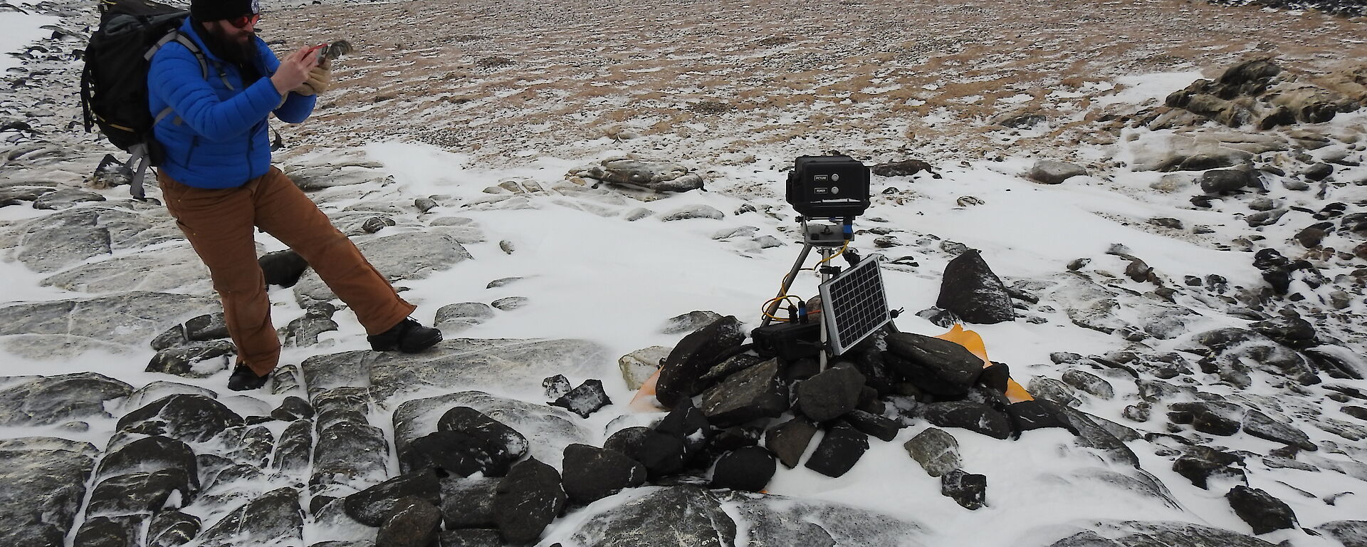 A man with a backpack checks an automated camera that sits out in the field