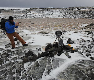 A man with a backpack checks an automated camera that sits out in the field