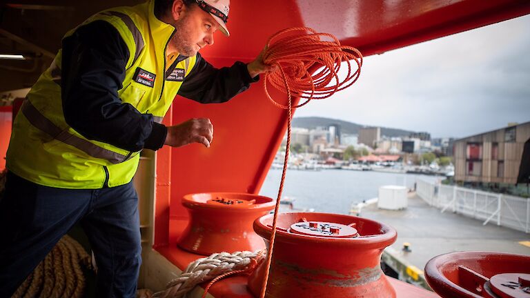 Crew about to throw a rope from the ship to the wharf.