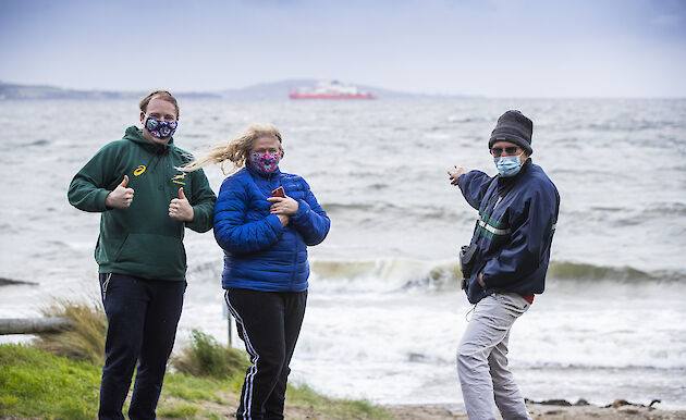 Three people giving the thumbs-up to the camera, with the RSV Nuyina in the background.