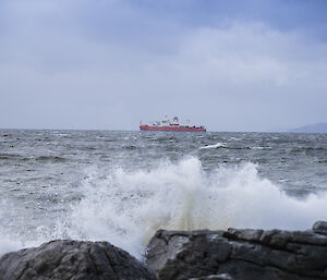 Waves breaking on rocks in the foreground; RSV Nuyina in the background
