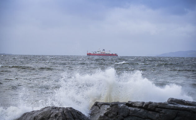 Waves breaking on rocks in the foreground; RSV Nuyina in the background