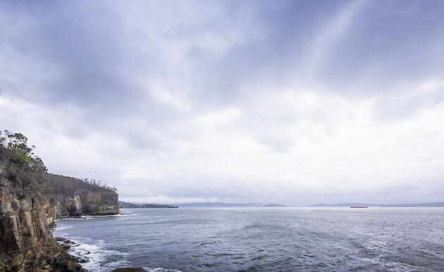 Cliffs and dramatic sky, with Nuyina small in the background