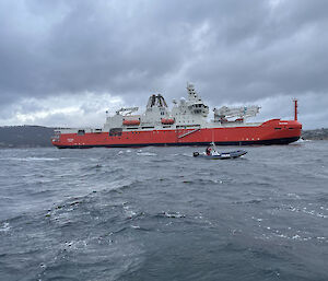 Big red ship sailing on river with smaller watercraft sailing alongside
