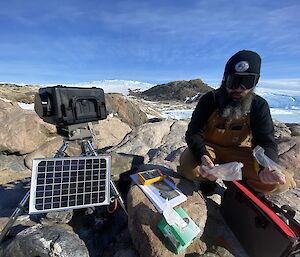 Expeditioner kneeling down working on rocks servicing remote penguin camera