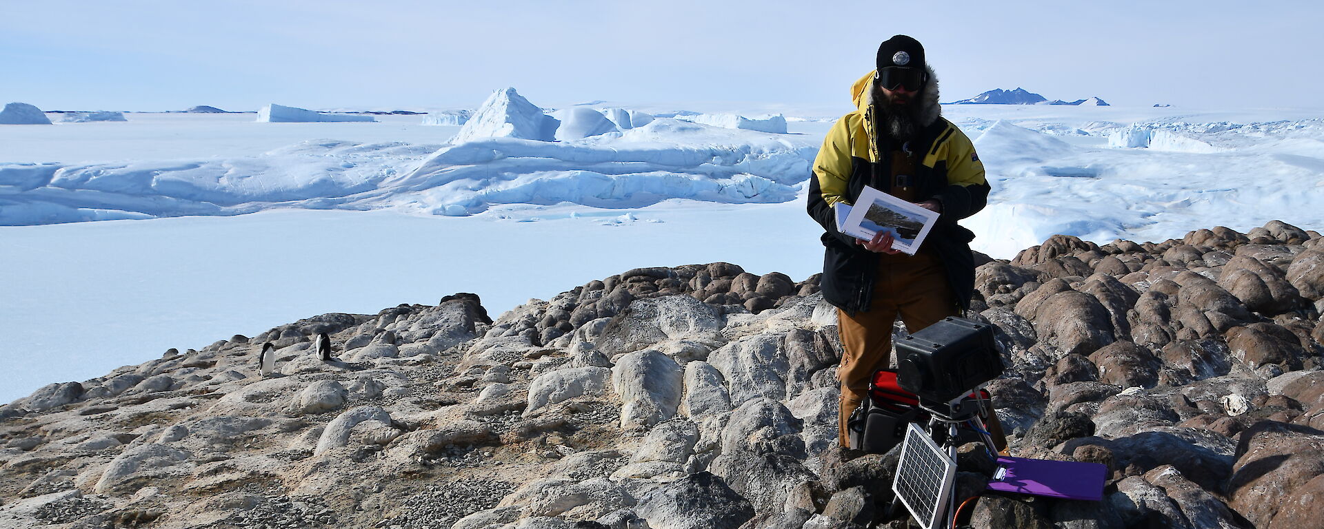 Expeditioner standing at remote camera with views of icebergs and Mount Henderson in distance