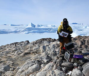 Expeditioner standing at remote camera with views of icebergs and Mount Henderson in distance