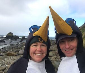 Two people dressed in penguin suits standing by the rocky shore