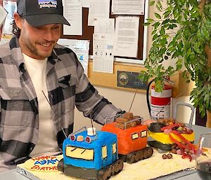 Birthday cake in the shape of a blue and orange Hagglund over snow vehicle towing a yellow sled.
