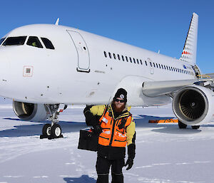 A man in front of a plane on an ice runway, carrying a cool bag away from the plane