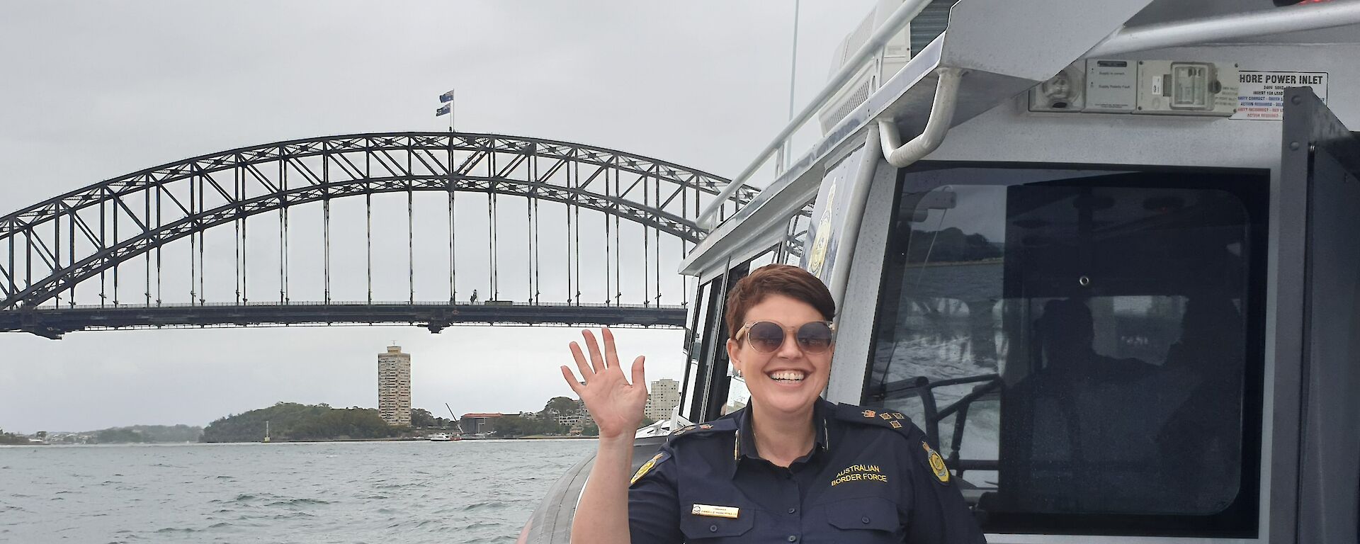 A woman waves from a boat with Sydney Harbour Bridge behind her