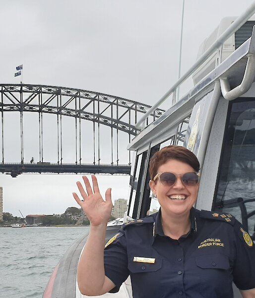 A woman waves from a boat with Sydney Harbour Bridge behind her