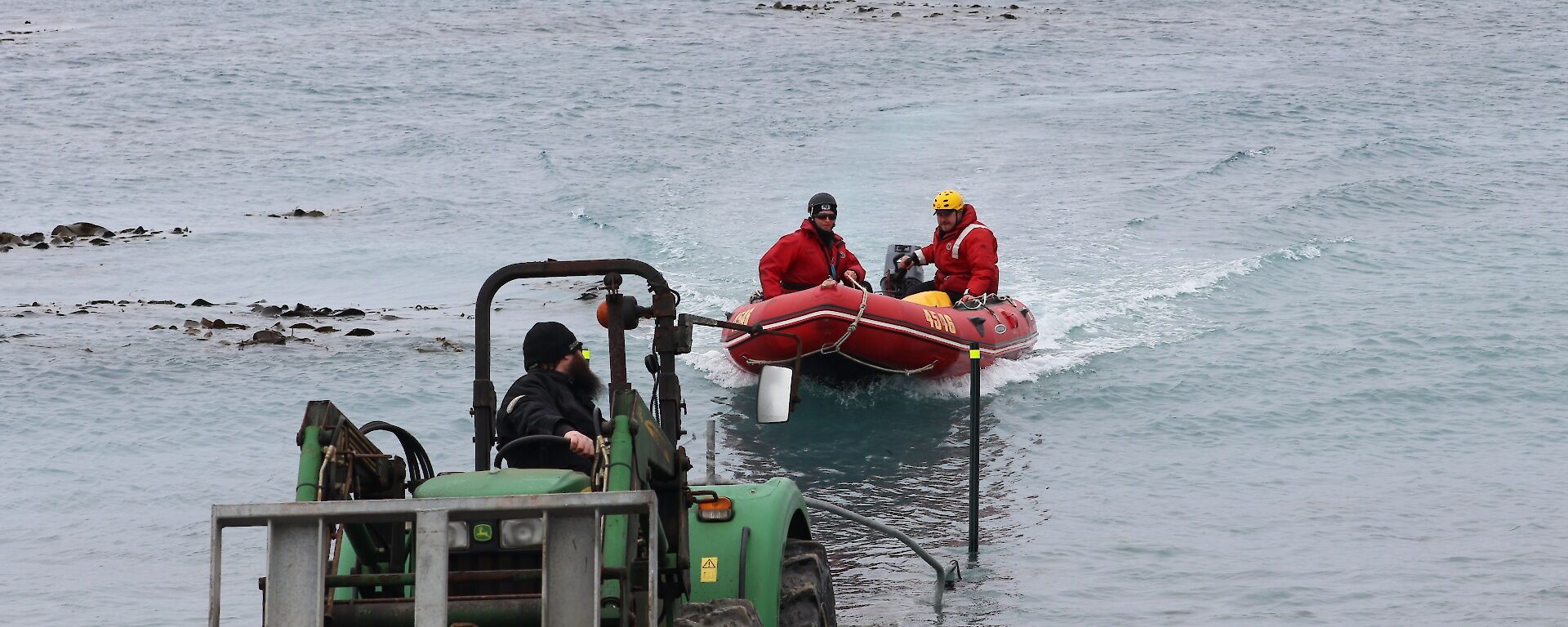People in a red rubber boat being pulled up the beach by a green tractor