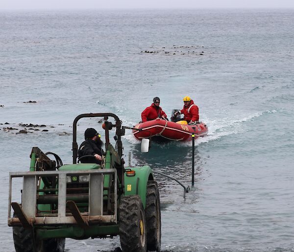 People in a red rubber boat being pulled up the beach by a green tractor