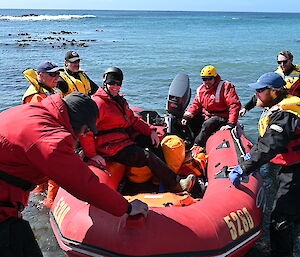 A red dinghy being pulled towards shore by a group of people in life jackets