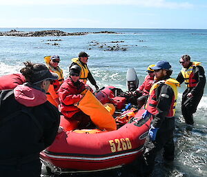 A red dinghy being pulled towards shore by a group of people in life jackets