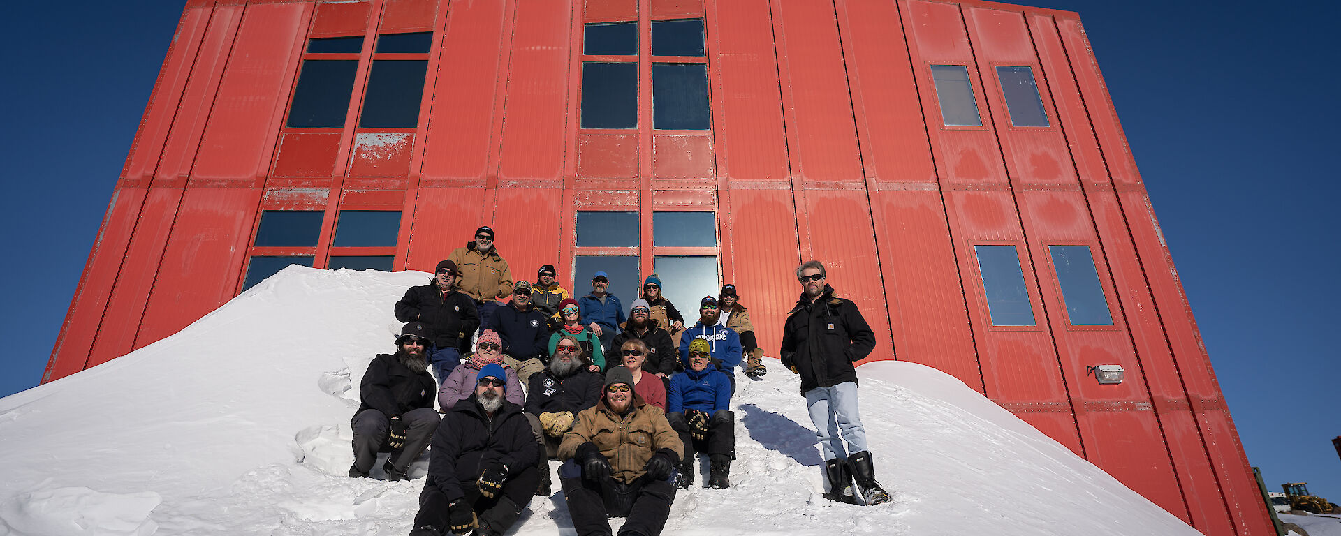 Group of expeditioners sitting on a sloped blizz tail in front of a red building