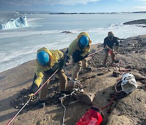 Three expeditioners pulling on the raise rope during a stretcher raise exercise.  Sea ice is visible below them.