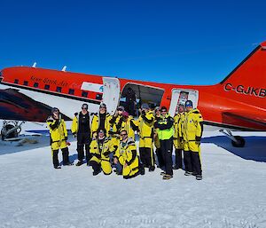 A group of expeditioners in yellow survival clothing standing outside a Basler aircraft