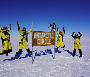 Four woman jumping with excitement next to the Antarctic Circle sign
