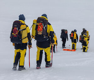 A group of expeditioners with field packs walking across the snow