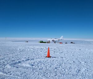 A plane sits in the distance on an ice runway with Hagglunds in front and marker cones on the snow in the foreground