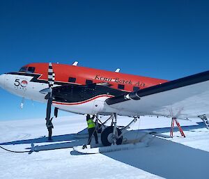 A red DC-3 Basler parked on the snow with a person working underneath it