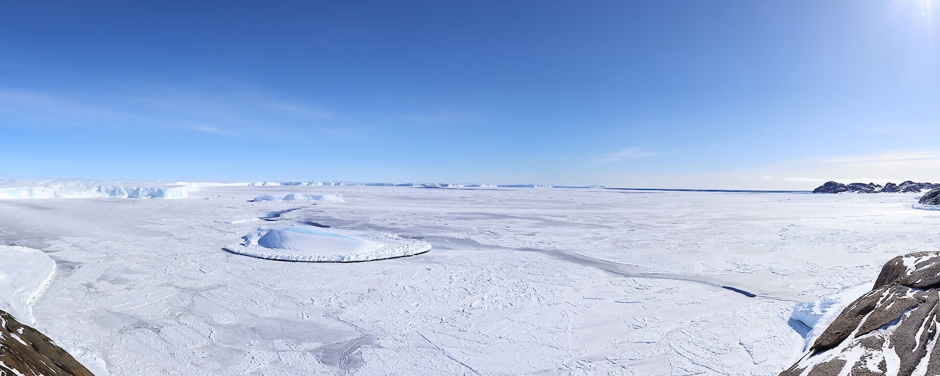 A panorama of the sea ice, nestled between two rocky hills.