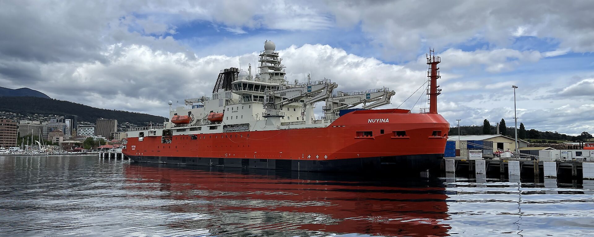 A large research ship tied up in docks with reflections on the water