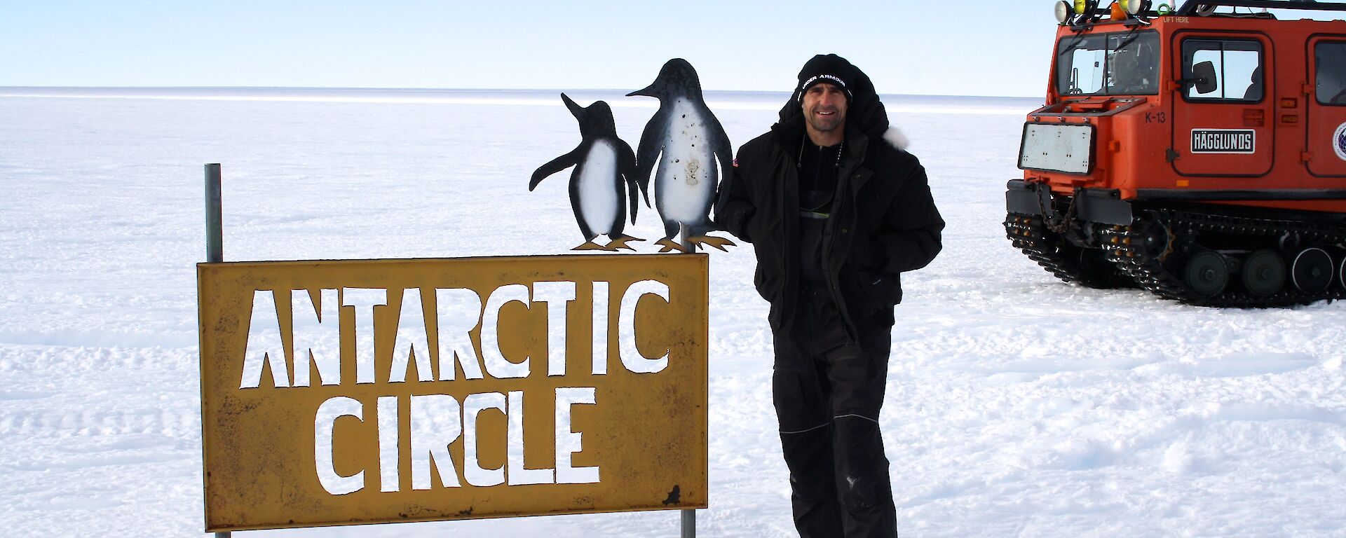 A man stands on the ice next to a sign