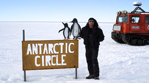 A man stands on the ice next to a sign