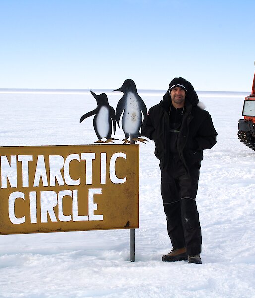 A man stands on the ice next to a sign