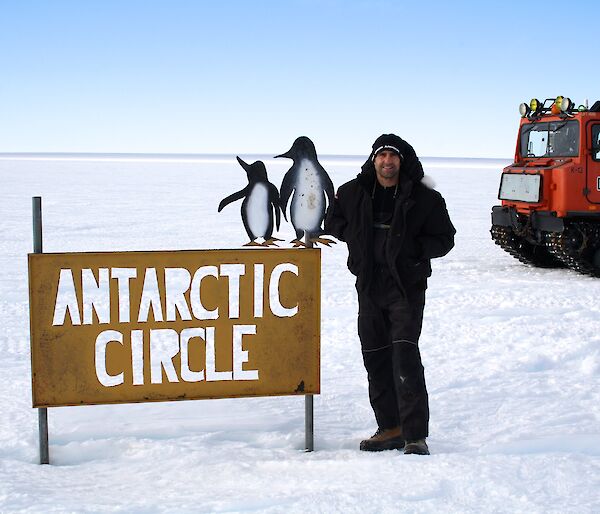 A man stands on the ice next to a sign