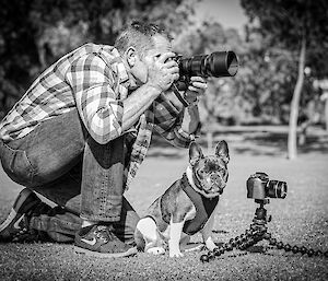 A man holds a camera next to a small dog