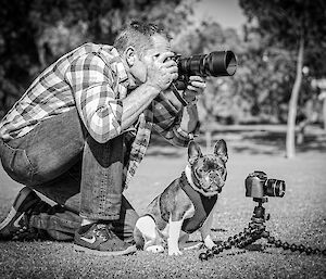 A man holds a camera next to a small dog