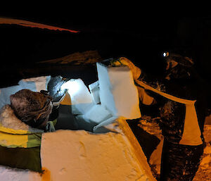 Two people building an igloo in the dark with their head torches on.