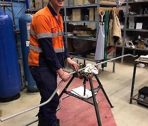 A man in hi-vis bending some electrical conduit in the workshop.