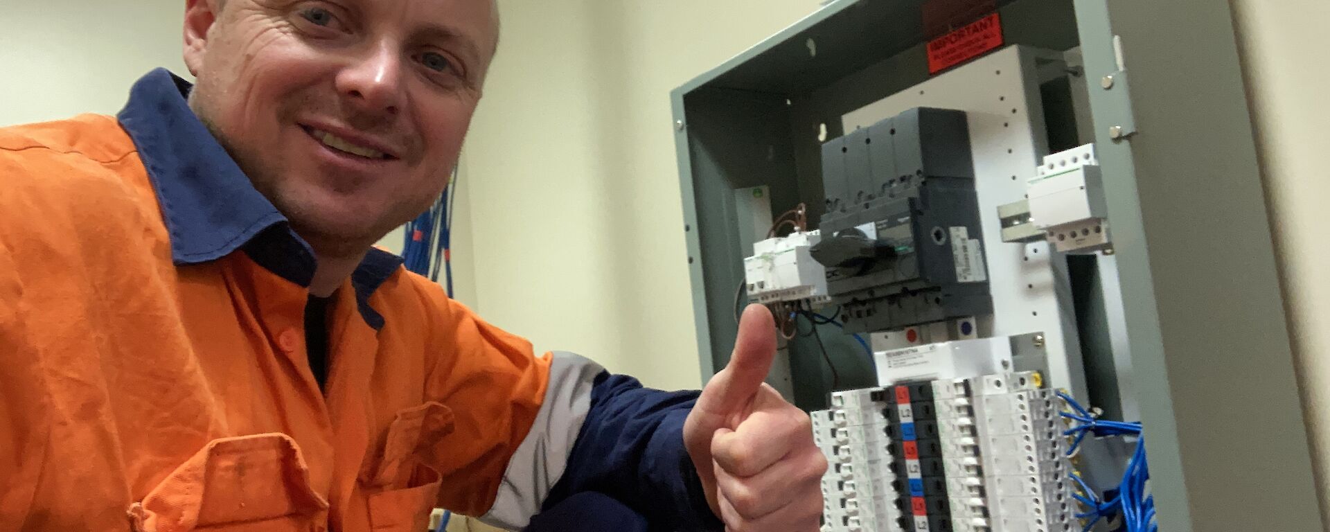 A man in hi-vis in front of the new switchboard give the thumbs up.