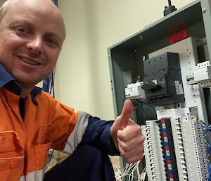 A man in hi-vis in front of the new switchboard give the thumbs up.