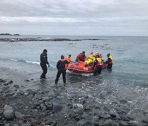 A group of people on the waterfront help guide a small red boat to shore