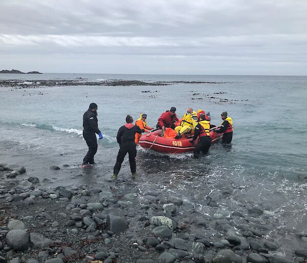 A group of people on the waterfront help guide a small red boat to shore